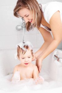 beautiful young mother washing her baby in the bath with foam (focus on the mother)